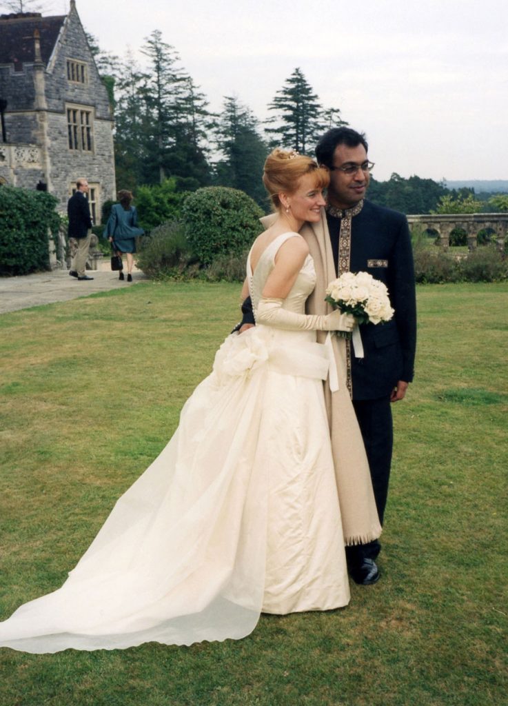 Bride wearing corseted bodice in silk duchess satin with covered buttons down the back, flared skirt with back overskirt train with silk organza rouched overlay flowing over the train by Joanna Bell